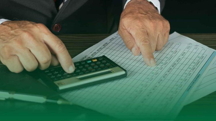 Mãos de pessoa usando calculadora e apontando para planilha de pagamentos, representando a análise de processos trabalhistas e controle financeiro empresarial.