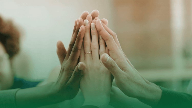 Pessoas em um sinal de colaboração, com as mãos para cima batendo um na mão do outros. Na imagem aparecem 4 mãos de pela branca e uma de pele negra.