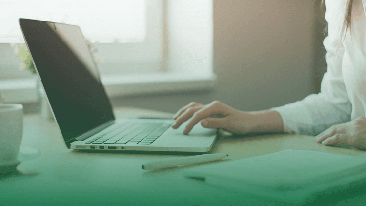 Pessoa usando notebook sobre uma mesa de trabalho, com caderno e caneta ao lado, representando o monitoramento digital e a análise de mídias negativas no contexto de compliance e gestão de riscos.