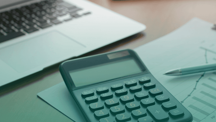 Notebook e calculadora sobre uma mesa de trabalho, representando controle financeiro, gestão de riscos e estruturação de processos de compliance.