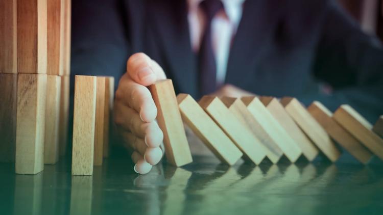 homem fazendo o possível para manter todas as peças do dominó em pé.